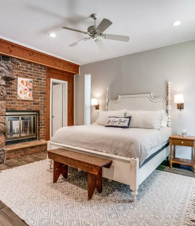 The primary bedroom with a queen size bed with a stone fireplace and ceiling fan.